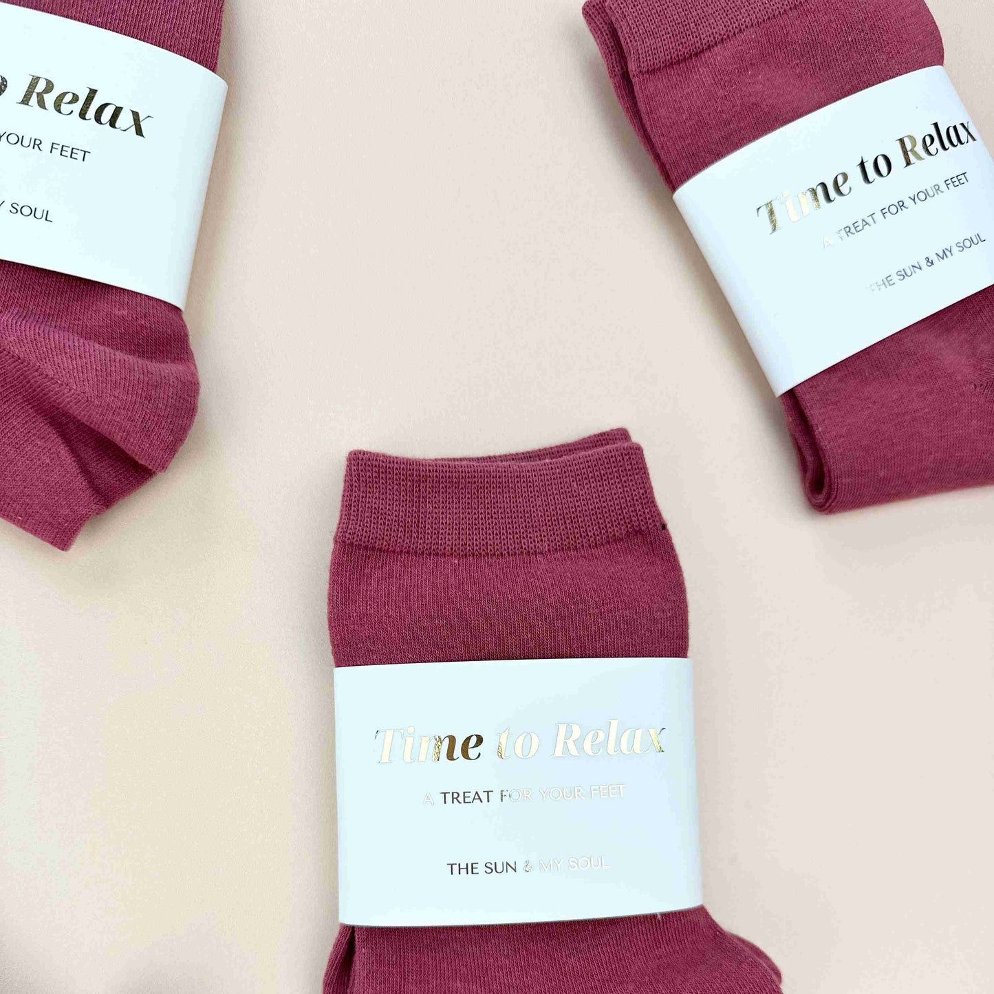 Maroon socks with 'Time to Relax' labels on a light pink background
