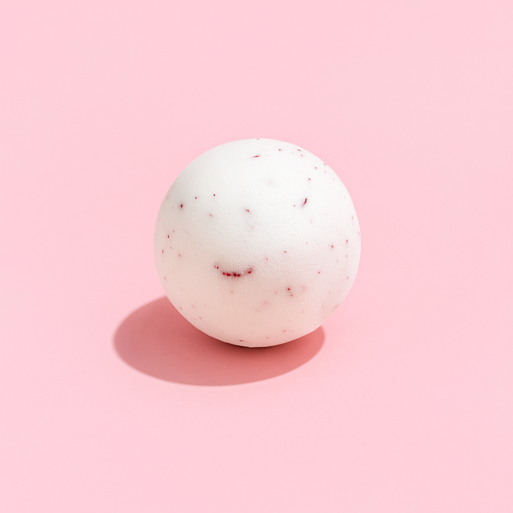 White bath bomb with red specks on a pink background