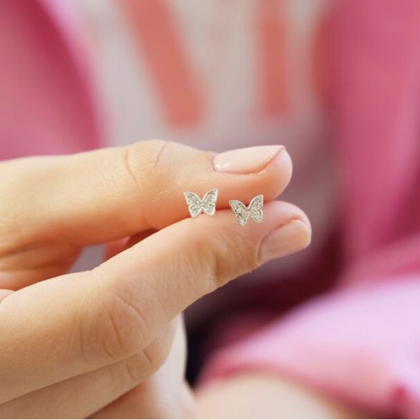 Butterfly-shaped earrings held between fingers against a blurred background