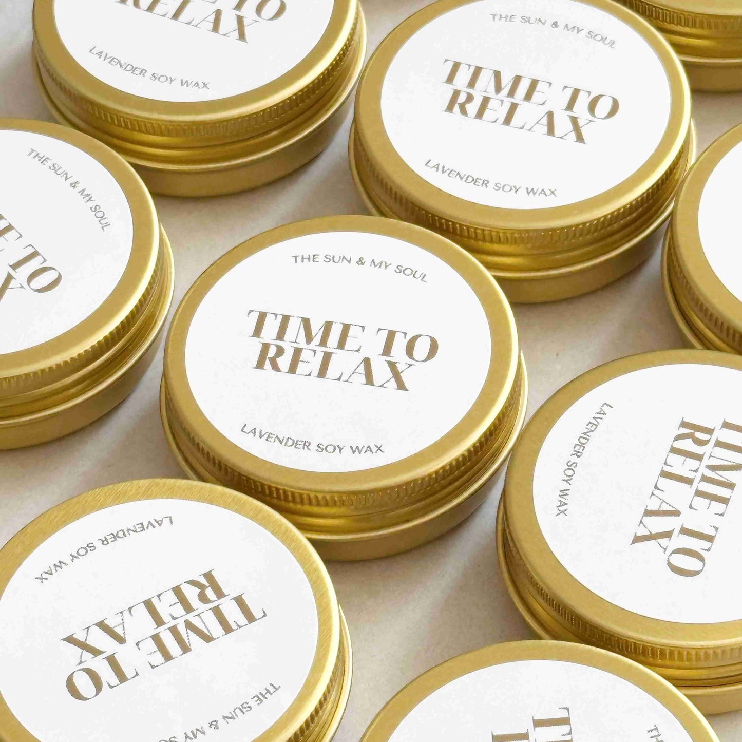Multiple tins of 'Time to Relax' candle with gold lids on a light background