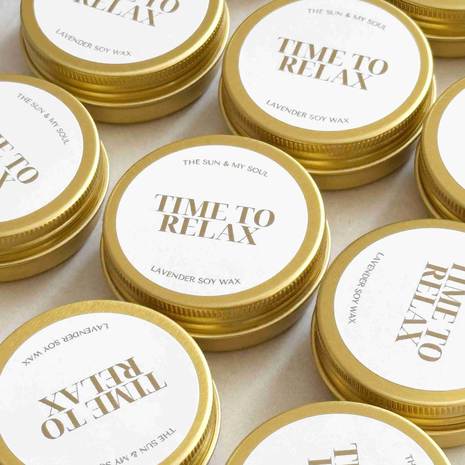 Multiple tins of 'Time to Relax' candle with gold lids on a light background
