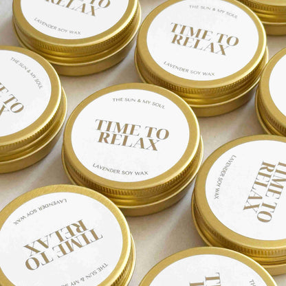 Multiple tins of 'Time to Relax' candle with gold lids on a light background