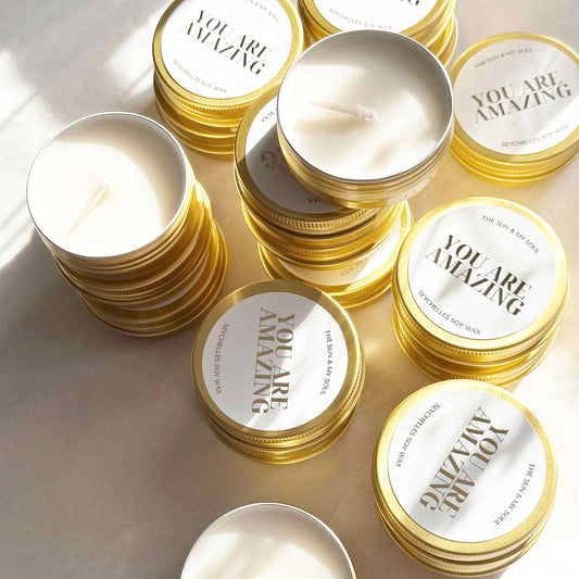 Candle tins with 'You Are Amazing' text on lids arranged on a light surface.