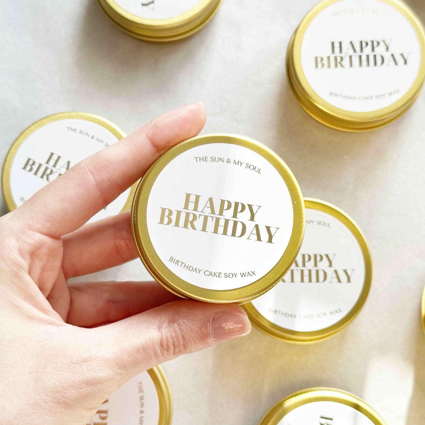 Hand holding a 'Happy Birthday' candle with more candles in the background on a light surface.