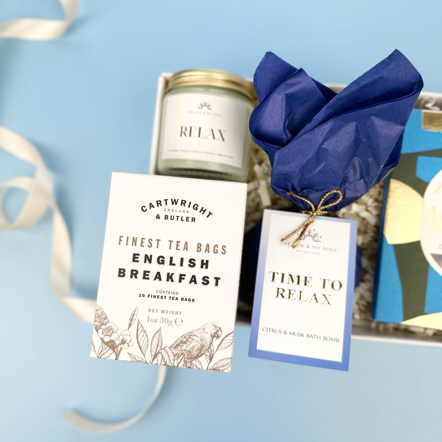 Tea set with 'Cartwright & Butler' tea bags and 'Riley' candle on a blue background