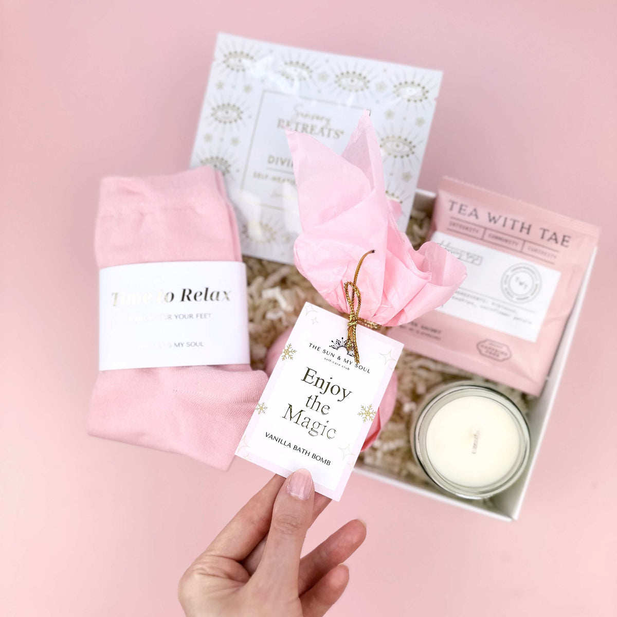 Pink gift set with socks, candle, and cards on a pink surface