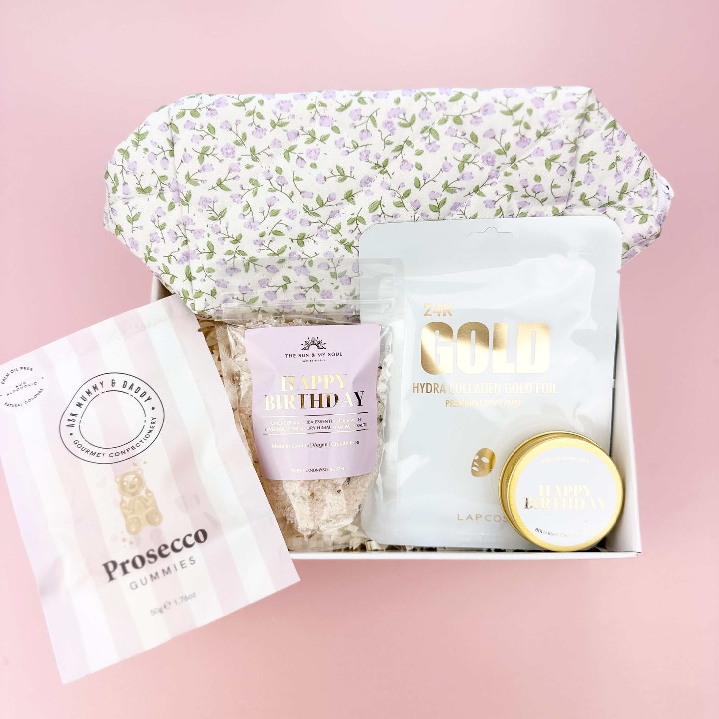 Gift set with a floral headband, bath bombs, and a Prosecco glass in a box on a pink background