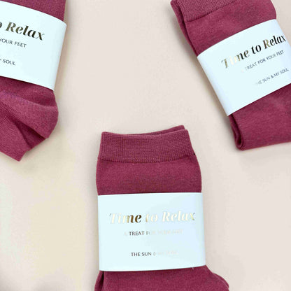 Maroon socks with 'Time to Relax' labels on a light pink background