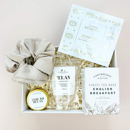 Gift box with tea bags, a scrunchie, and a small round item on a light background