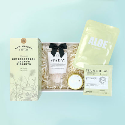 Gift set with Cartwright & Butler butterscotch crunch biscuits, a candle, and tea on a light blue background