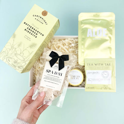 Hand holding a spa day gift set with various items on a light blue surface