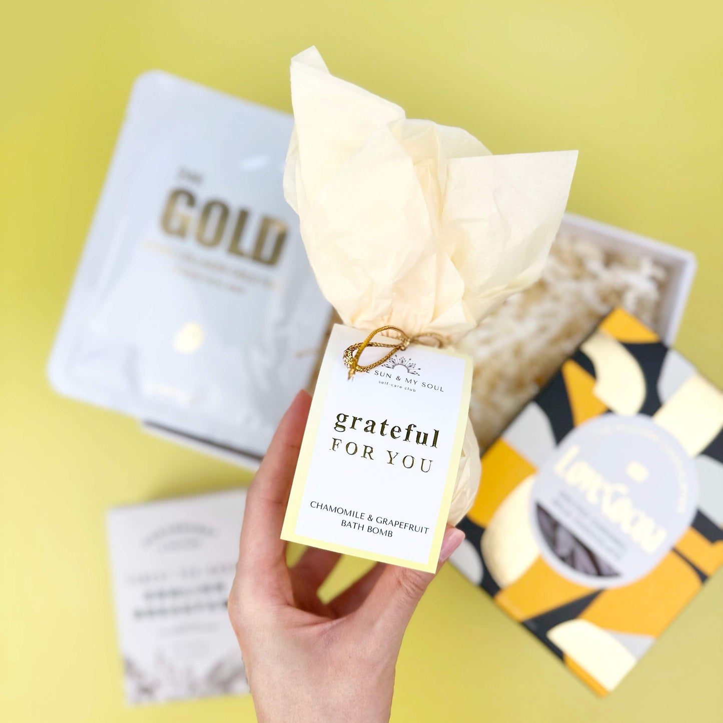 Hand holding a product with a 'grateful for you' tag against a yellow background