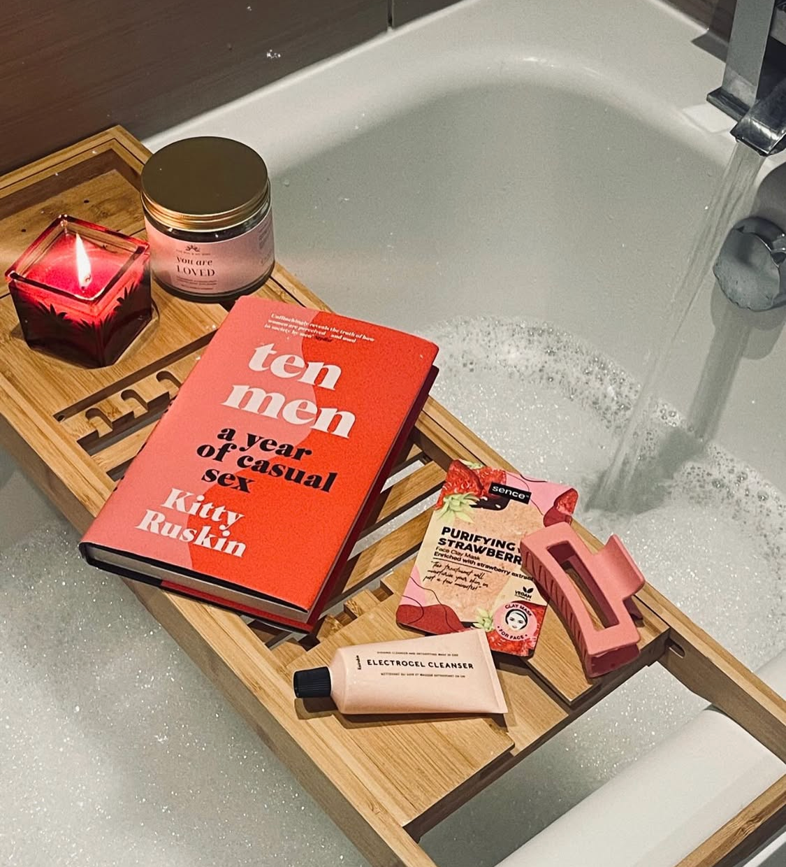Bath tray with books, soap, and candles by a sink