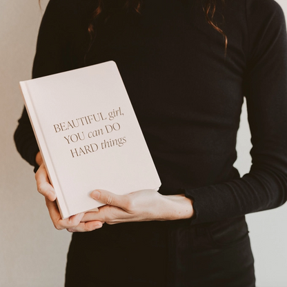 Person holding a book titled 'BEAUTIFUL girl, YOU can DO HARD things' against a neutral background