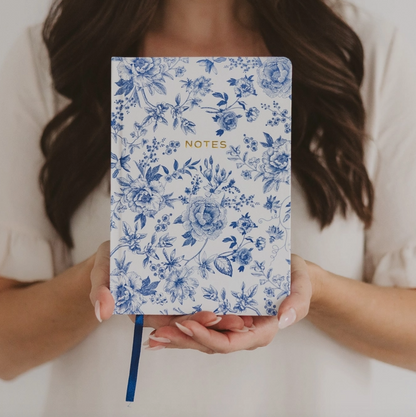Person holding a notebook with blue floral pattern and 'NOTES' text