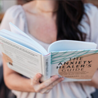 Person holding and reading 'The Anxiety Healer's Guide' book.
