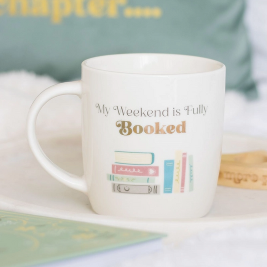 White mug with 'My Weekend is Fully Booked' text and book illustrations on a light background