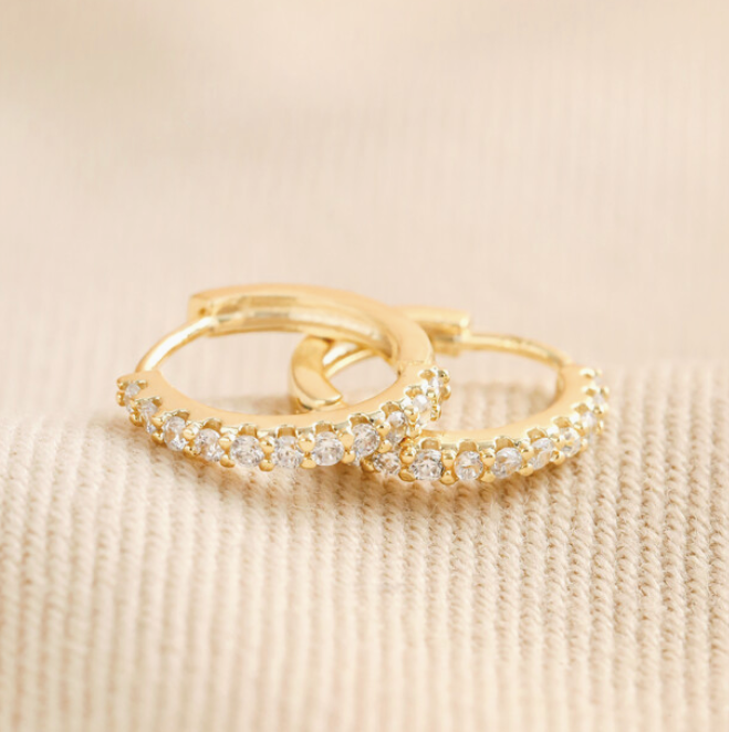Gold earrings with embedded diamonds on a beige fabric background