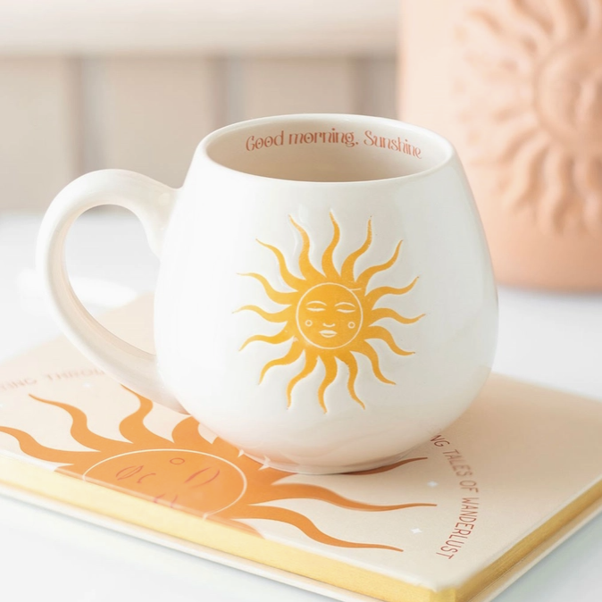 White mug with sun design and 'Good morning, Sunshine' text on a surface with a blurred background