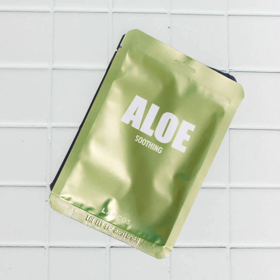 Green aloe vera sheet mask on a white tiled background