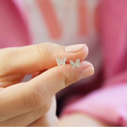 Butterfly-shaped earrings held between fingers against a blurred background
